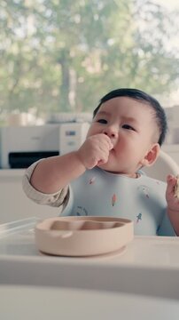 Asian Baby Using Finger to Feed Herself a Food with Baby Led Weaning Concept.Cute Asian baby boy eating finger food in high chair.