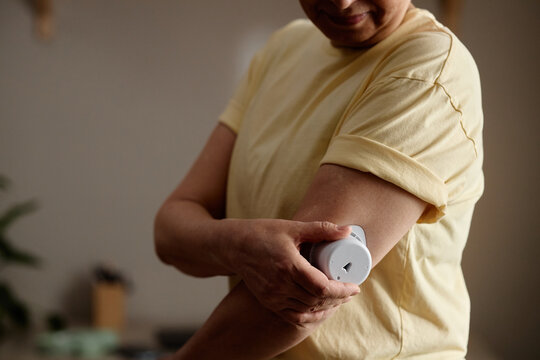 Asian middle aged woman applying wearable glucose monitor on upper arm, managing diabetes at home. Close up supporting healthcare marketing, chronic disease awareness, telehealth
