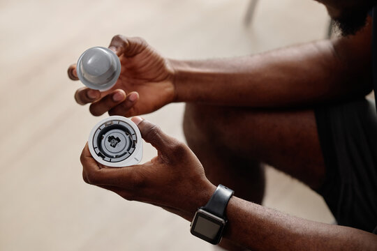 Close up of Black man holding insulin pump while sitting on sofa in living room. Ideal for IoT, insulin pump marketing 
