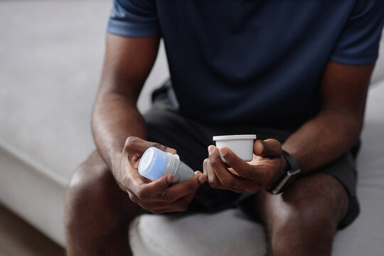 Close up of unrecognizable black man sitting on sofa and holding insulin pump. Ideal for healthcare, prescription use, self care marketing