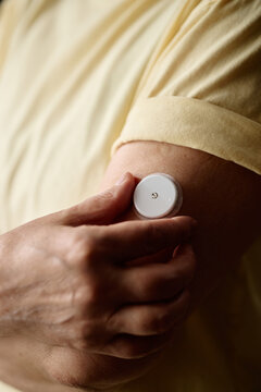 Vertical shot of middle aged woman adjusting continuous glucose monitor on upper arm, tracking diabetes treatment and health data. Ideal for healthcare, telemedicine, patient education