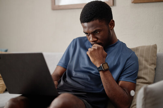 African American young adult man reviewing laptop screen while sitting at home, conveying remote work focus and problem solving. Useful for productivity, freelance and diabetes support