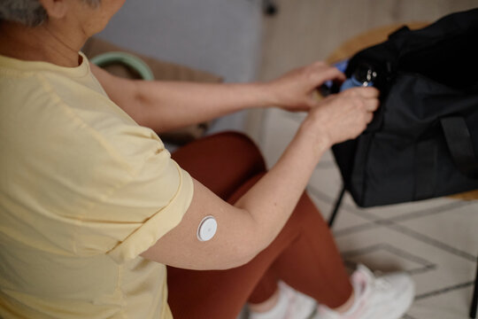 Senior woman with glucose sensor packing bag before leaving home, managing diabetes and daily routine. Useful for healthcare marketing, chronic condition awareness, patient support