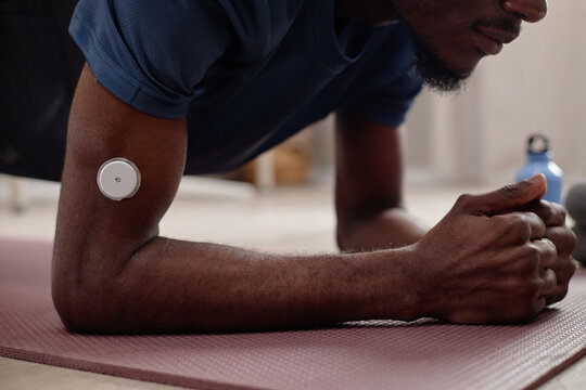Close up of young adult Black man holding plank on exercise mat, wearing glucose monitor for diabetes tracking and fitness routine. Ideal for wellness, health tech, chronic care marketing