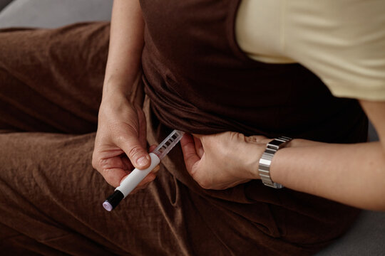Close up of woman injecting abdomen with insulin pen, managing diabetes treatment at home. Suitable for healthcare campaigns, chronic disease education, patient support