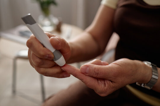 Close up of woman pricking fingertip with glucose meter lancet, monitoring blood sugar for diabetes management. Ideal for healthcare, chronic condition, wellness campaign use