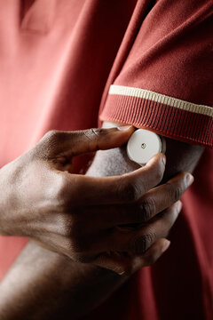 Vertical shot of Black man adjusting wearable glucose monitor on upper arm, managing diabetes treatment and health tracking. Ideal for medical technology, chronic care, insurance campaigns
