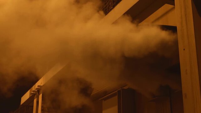Nighttime sequence of thick amber smoke pouring from building eaves and expanding outward under
