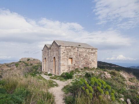 Ancient stone church ruins in Paleochora, the medieval capital of Aegina Island, Greece. Historic Byzantine architecture on a hilltop overlooking the sea and mountains under a cloudy sky.