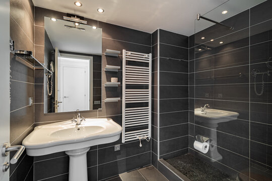 Modern bathroom with sleek black tiles, a white sink, and a glass shower. Bright lighting enhances the contemporary design.