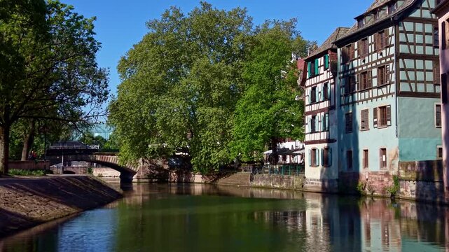 Low drone glides over Ill canal in Petite France, colorful timber-framed houses and bridge