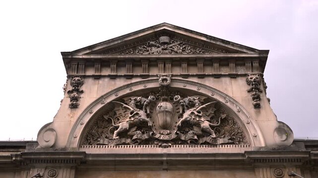 Intricate stone carvings and crest fill the pediment of Smithfield Market&rsquo;s historic facade under an overcast sky.