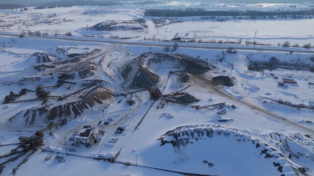 Large winter gravel quarry with snow covered mounds, conveyors and access roads seen from above.