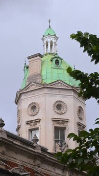 Ornate Smithfield Market tower with green dome rises behind leafy tree branches on an overcast London day.