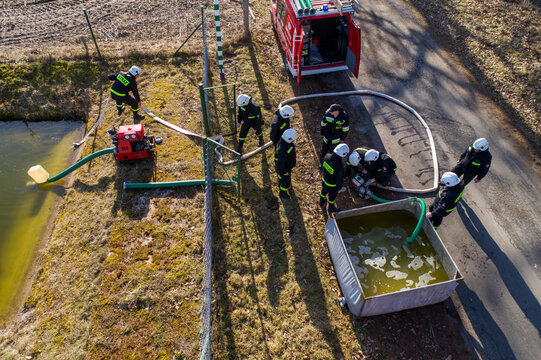 Aerial view of firefighters operating a water pump and hoses near a pond and a portable tank during an exercise in Debrzno, Pomeranian Voivodeship, Poland.