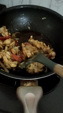 wooden spatula stirring diced chicken and onions in a hot wok.