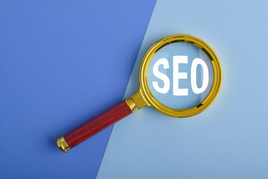 Magnifying glass highlighting SEO text on blue background with copy space. Concept of search engine optimization, digital marketing, online visibility, keyword research and web analytics.