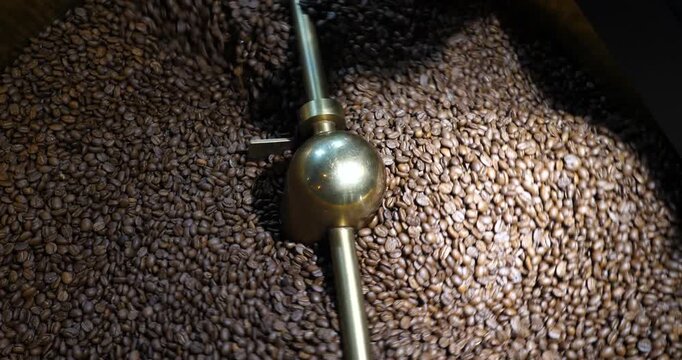 Process of mixing and grinding roasted coffee beans, aromatic brown coffee beans rotating,mixing machine mixes roasted coffee beans in roaster, close up