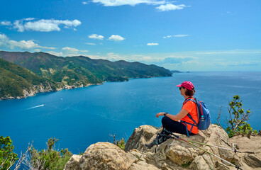 Obraz premium Active senior woman hiking hike above Monterosso ,Cinque Terre, Panoramic view of the Mediterranean Sea, dramatic coastline, lush hills, and picturesque village , Cinque Terre, Liguria, Italy. 