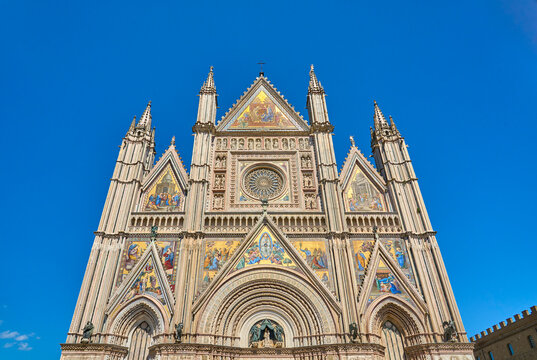  Orvieto Cathedral in Umbria, Italy, showcasing its ornate Gothic facade, colorful mosaics, rose window, and detailed stone carvings under a clear blue sky.