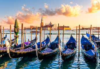 row of parked venetian gondola boats in Grand canal of Venice. Beautiful sunset or sunrise landscape with gondolas in blue water of Venice. © Yaroslav