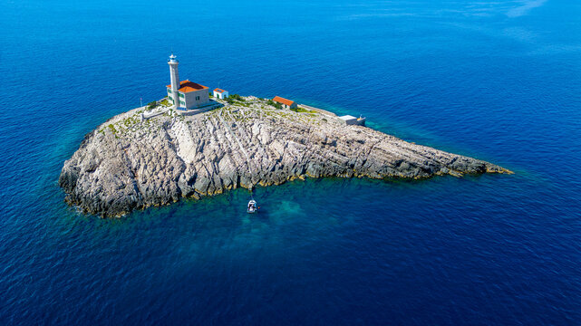 Aerial view of Blitvenica Lighthouse on a small rocky island surrounded by the deep blue Adriatic Sea with a small boat anchored nearby Zirje, Sibensko-kninska zupa, Croatia.