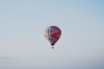 Fototapeta premium Colorful hot air balloon floating above the morning mist with a pastel blue sky