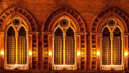 Obraz premium old yellow facade of house with three brown vintage windows in retro gothic italian european style. Night italian architecture.
