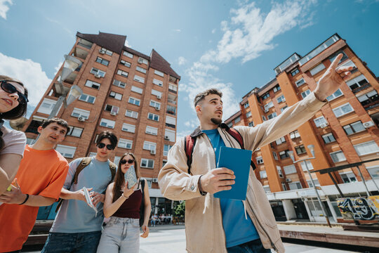 A group of students listening to a guide pointing toward buildings. The young adults stand outdoors on an urban campus tour, looking in the same direction.