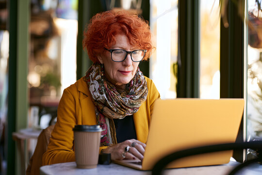 Mature woman working remotely from a coffee shop with a laptop and a takeaway coffee