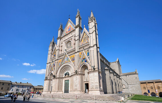 Orvieto Cathedral in Umbria, Italy, showcasing its ornate Gothic facade, colorful mosaics, rose window, and detailed stone carvings under a clear blue sky.