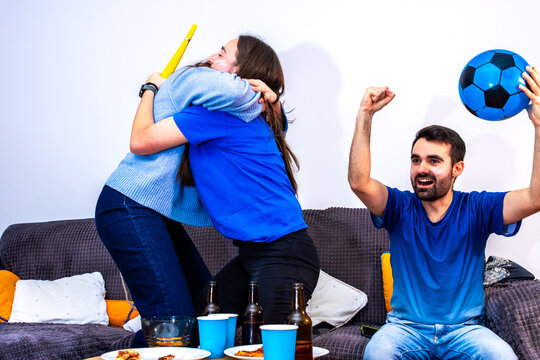 Excited friends watching a football game at home, celebrating a significant moment
