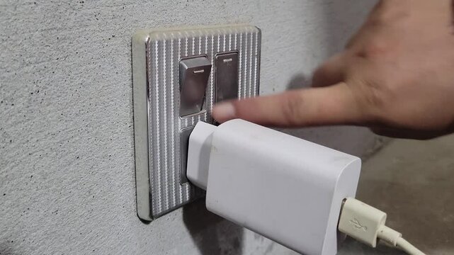Person plugging a mobile charger into a wall socket and turning on the switch