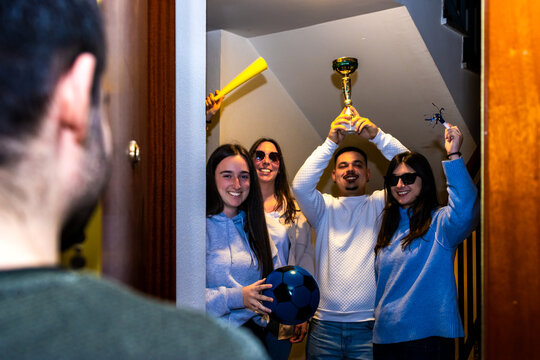 Friends celebrating a soccer victory, holding a trophy, ball, and sports fan items