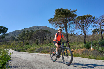 Fototapeta premium Active senior woman riding an electric mountain bike on a scenic road up to Mount Vesuvius in Pompei, Campania, Italy.