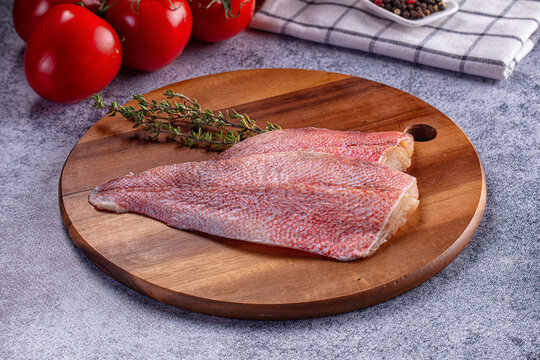 Raw red snapper fillets with fresh thyme and tomatoes on wooden board