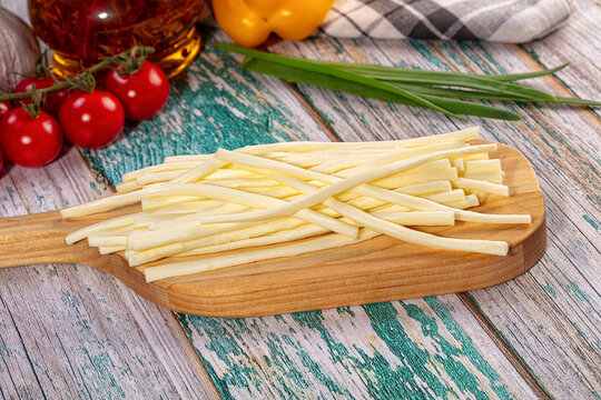 Sliced string cheese sticks on wooden board with fresh vegetables