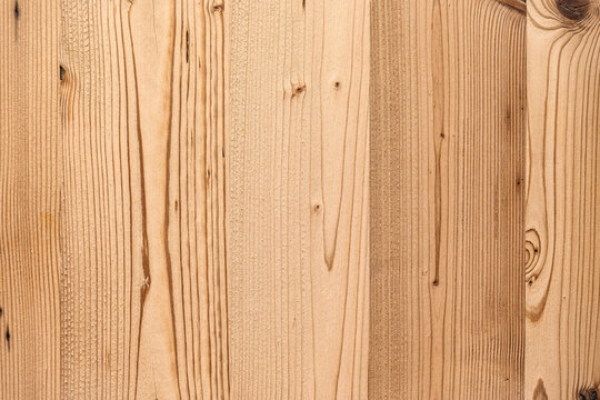 Detailed view of a wooden wall paneling surface composed of vertical planks in light to medium brown, with a warm, natural tone. The grain of the wood is prominently displayed.