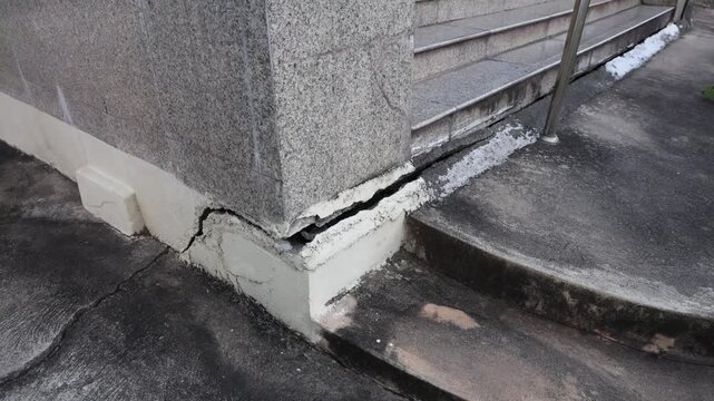 Camera pans to show cracks in the concrete at a building entrance. The damage can be seen on the surface and around the steps. This issue may need repair work.