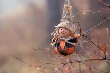 Fototapeta premium autumn nature background with cute funny scarecrow figurine close up. scarecrow smiling doll on tree branch outdoor. festive decor for fall season. symbol of harvest, autumn, Halloween