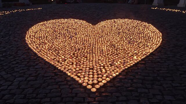 Heart-shaped arrangement of lit tea candles on cobblestone pavement at twilight