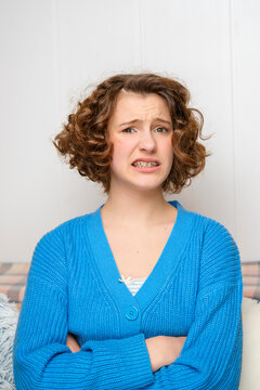 young teenage girl with braces making a disgusted face, showing repulsion and discomfort while crossing her arms, isolated on a white studio background