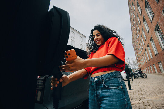 Electric mobility as a woman charges her car on an urban street
