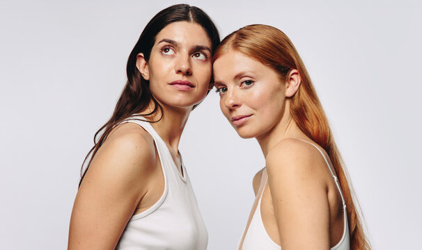 Two women in studio leaning close with glowing skin