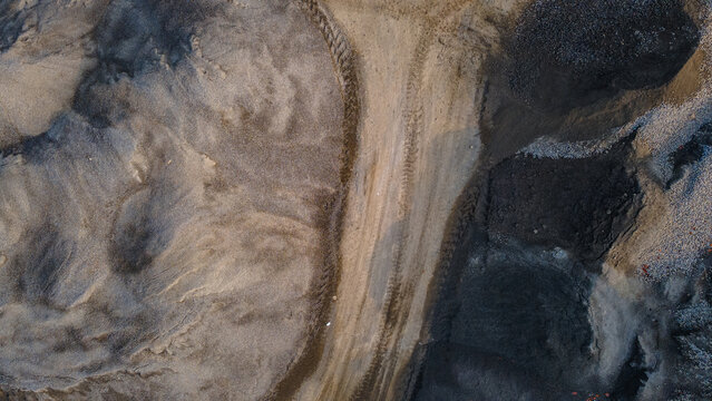 Aerial view of a quarry site with piles of sand, gravel, and dark soil featuring heavy machinery tire tracks in Karanglewas, Central Java, Indonesia.