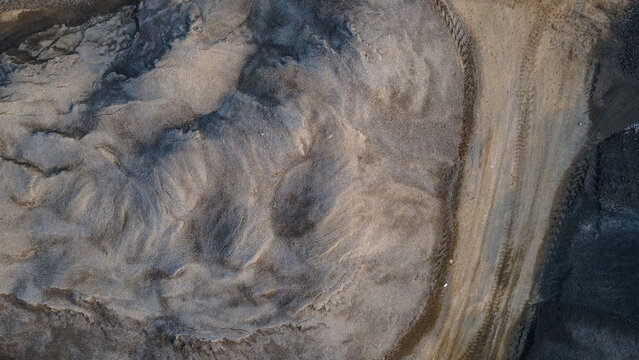 Aerial view of a sand quarry with mounds of aggregate and heavy machinery tire tracks in Karanglewas, Central Java, Indonesia.