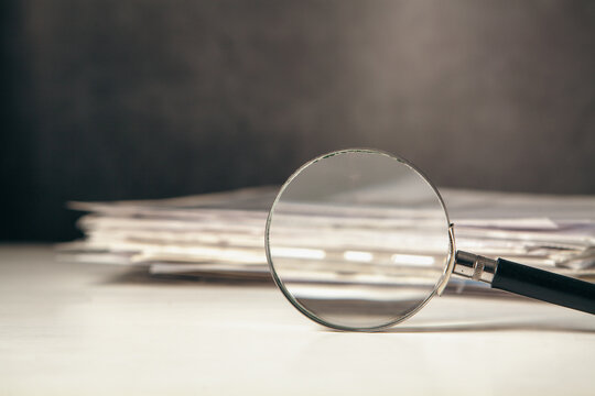 Magnifying glass on a pile of documents. Selective focus.