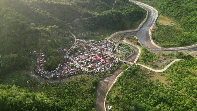 A sweeping aerial drone video orbits Obi village in lush Caramoran, Catanduanes, Philippines, revealing rural roads, river, and tropical greenery bathed in sunlight.