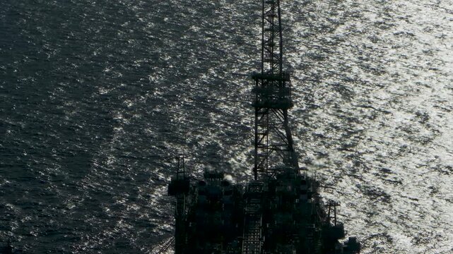 Cinematic close-up aerial footage focusing on the burning gas flare stack of an industrial offshore oil platform set against the backdrop of open deep sea waters.