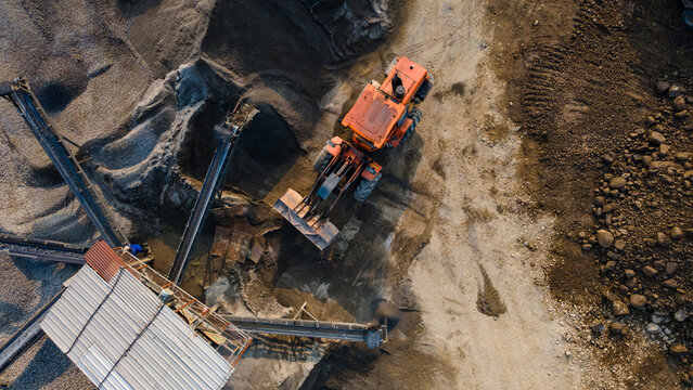 Aerial view of an orange wheel loader working near a conveyor belt at a sand quarry with piles of gravel in Karanglewas, Central Java, Indonesia.